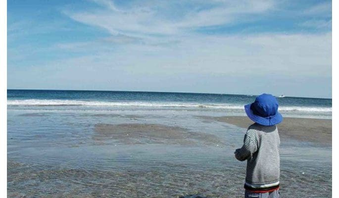 A child standing on the beach looking at the ocean.