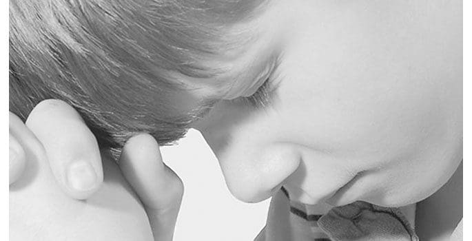 A young boy is looking down at his ear.