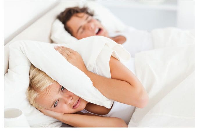 A woman and man laying in bed with pillows on their heads.